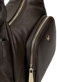 Brązowa skórzana torba na ramię o teksturowanym wykończeniu, z podwójnymi zamkami i złotym akcentem w postaci logo. Kompaktowy design z zaokrąglonymi krawędziami.