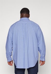 Jasnoniebieska koszula w kratę z kołnierzykiem na guziki. Długie rękawy i boczne rozcięcia. Miękka tekstura, luźny krój. Widoczne detale przeszyć.