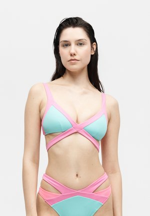 Γυναίκα με βρεγμένα σκούρα μαλλιά φοράει μπικίνι πάνω μέρος σε παστέλ μπλε και ροζ με λουράκια και ταιριαστό κάτω μέρος σε λευκό φόντο.