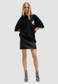 Un tricou oversized negru cu un grafic alb, asociat cu o fustă mini din piele neagră, care se potrivește pe corp, și cizme argintii lucioase până la gleznă.