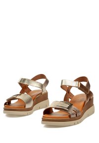 Sandalias de cuña con tiras metálicas en oro y bronce, un upper texturizado, una plantilla de cuero suave y una suela de goma de color claro.