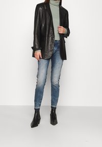 Černá kožená blazer, zelený rolák, světle modré džíny a černé kotníkové boty. Texturovaná látka a střižený design s uvolněným střihem.