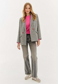 Šedý houndstooth blazer s červenými knoflíky, růžový svetr a šedé zvonové džíny, doplněné světle šedými teniskami. Hladká textura po celé ploše.
