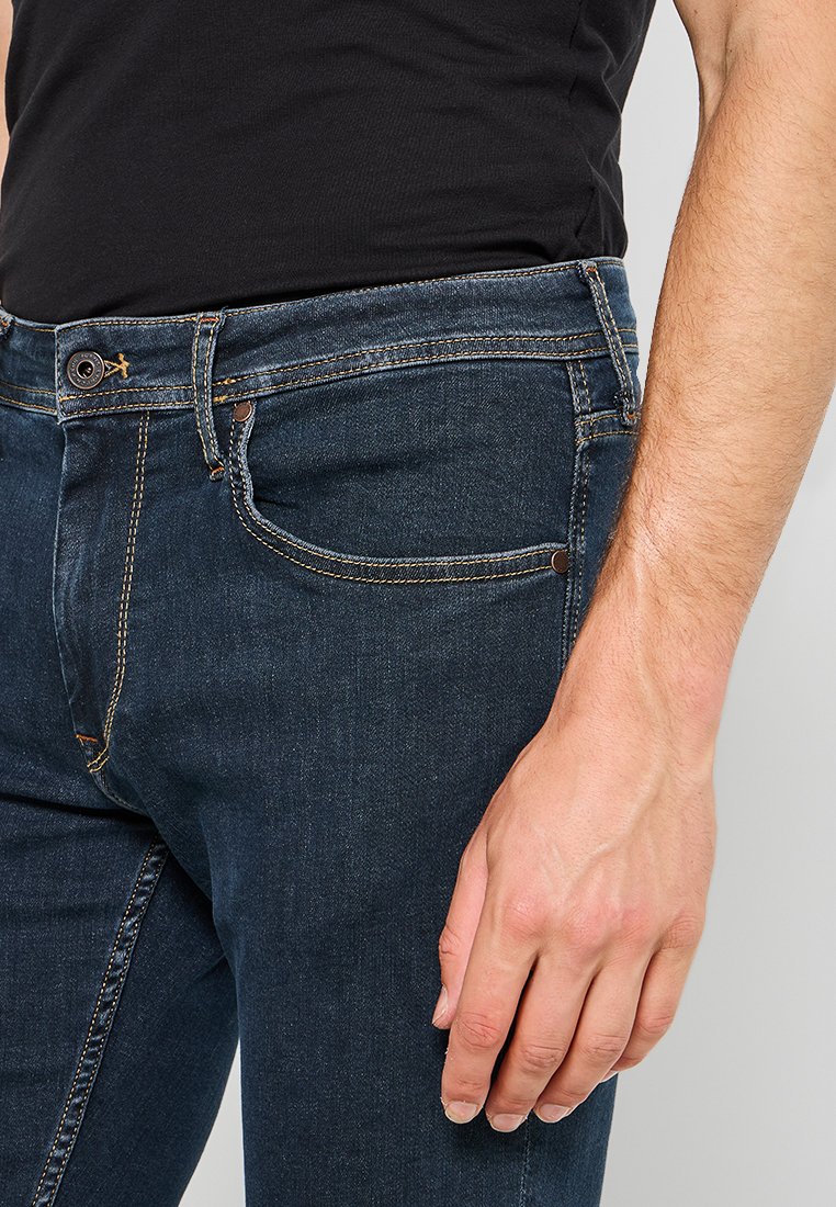 Dunkelblaue Jeans mit schmaler Passform, aus Denim gefertigt. Verfügt über einen Knopfverschluss, Gürtelschlaufen und gelbe Nähte entlang der Nähte.