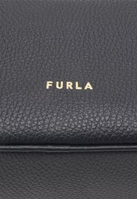 Czarna torebka skórzana o teksturowanej powierzchni z złotym logo "FURLA". Charakteryzuje się gładkim, usztywnionym kształtem oraz widocznymi detalami przeszycia.