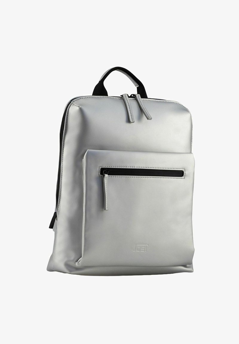 Sac à dos argenté en matériau synthétique lisse ; dispose d'une poche zippée à l'avant et de deux poignées supérieures, avec un design minimaliste.