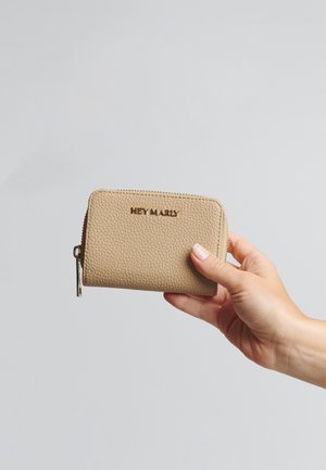 Portefeuille en cuir beige avec une surface texturée, arborant un logo doré "HEY MARLY", une fermeture éclair et tenu dans une main.