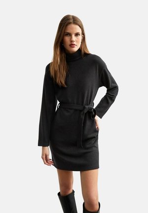 Vestido de punto negro con cuello vuelto, mangas largas, cinturon en la cintura y corte recto, combinado con botas negras hasta la rodilla.