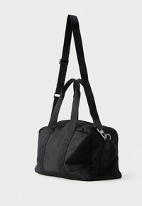 Fekete nylon sporttáska kétszeres fogantyúval és levehető vállpánttal. Simaszerkezet jellemzi, ezüst hardware kiegészítőkkel.