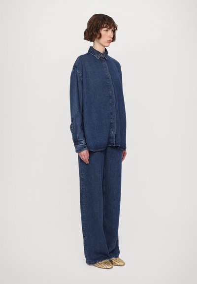 Oversized denim shirt with a pointed collar, button closure, and long sleeves, paired with wide-leg denim pants in a dark blue wash.