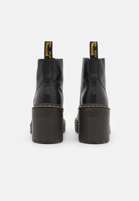 Svarta läderanklar med en kraftig ribbad sula, gula sömmar som accentuerar, och dragflikar med kontrasterande text vid hälen.