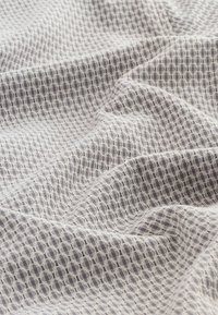 Tissu doux et froissé avec un motif géométrique hexagonal gris et blanc à petite échelle, montrant la texture et des plis.