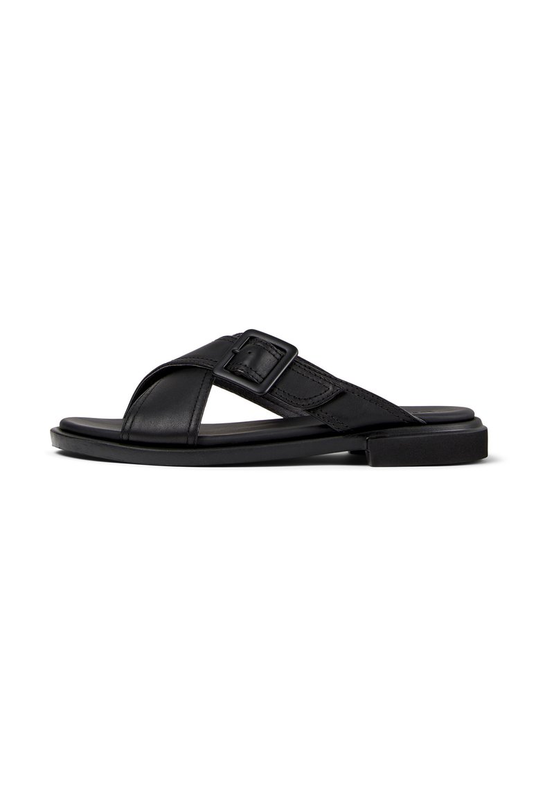 Black leather sandal with cross straps, buckle detail, flat sole, and smooth texture. Simple design with a minimalist aesthetic.
