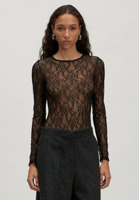 Zwarte kanten bodysuit met lange mouwen, bloemenpatronen en een ronde halslijn, gecombineerd met hooggepriceerde donkere textuurbroeken.