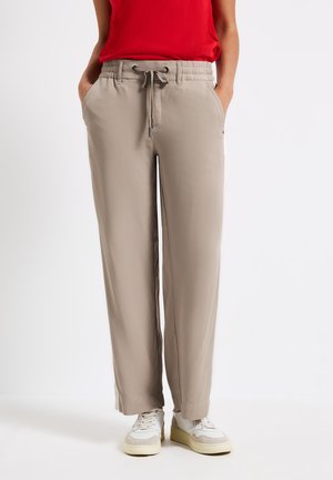 Beige wijde broek met een elastische tailleband en trekkoord. Voorzien van zijzakken en een gladde textuur, gecombineerd met witte sneakers.