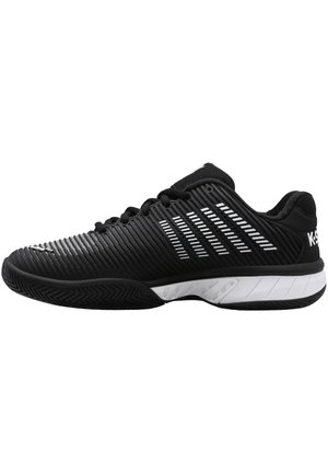 Chaussure de sport noire avec une tige texturée, ornée de rayures blanches diagonales et d'une semelle blanche contrastante. Conçue pour la performance et la stabilité.