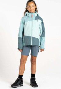 Helleblaue und dunkelgraue wasserdichte Jacke mit Kapuze, mit Reißverschluss vorn, elastischen Bündchen, getragen über grauen Shorts und schwarzen Wanderschuhen.