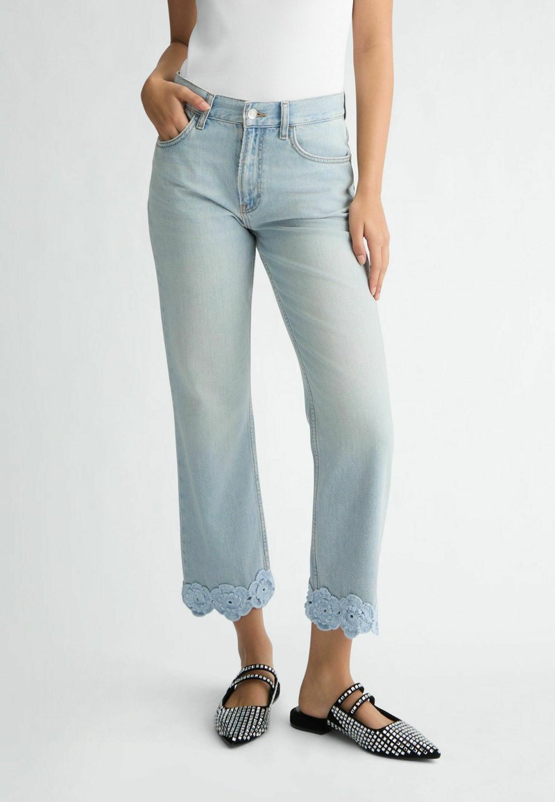 Jeans en denim bleu clair avec des jambes droites et des bordures en dentelle florale à l'ourlet. Associés à des ballerines noires avec des accents en strass.