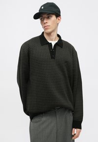 Μαύρη και γκρι πουλόβερ με σχέδιο και μαύρο γιακά, τρία κουμπιά και μακριά μανίκια. Συνδυάζεται με γκρι παντελόνι με ρίγες.