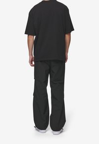 Czarny bawełniany T-shirt o luźnym kroju, zestawiony z czarnymi spodniami cargo z kieszeniami. Obydwa elementy charakteryzują się prostym designem i kolorem.