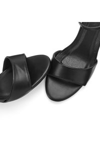 Black leather heeled sandals featuring a wide crossed strap design, smooth texture, open toe, and a slim ankle strap.