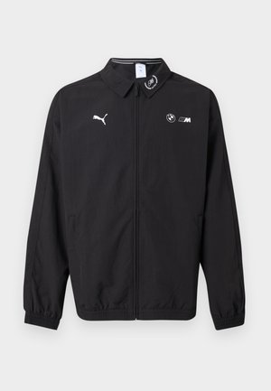 Čierna bunda na zips s logom Puma na ľavej strane hrude, logom BMW M na pravej strane hrude, elastickými manžetami a malým emblémom na golieri.