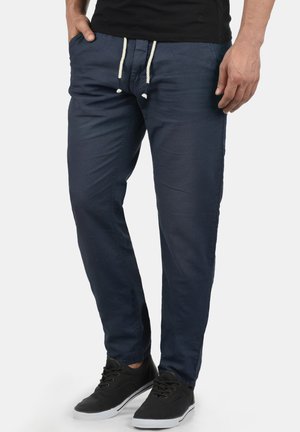 Pantalons joggers en coton bleu marine avec taille à cordon de serrage, deux poches latérales et design fuselé. Portés avec des baskets noires.