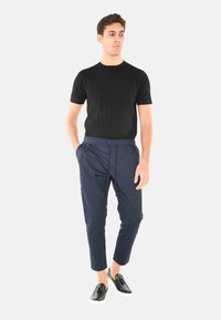 Maglietta nera a righe con maniche corte abbinata a pantaloni tapered blu con vita elasticizzata e scarpe slip-on nere con suola bianca.