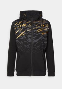 Haut à capuche noir à fermeture éclair avec capuche et cordons, présentant des motifs abstraits de rayures de tigre gris et or, ainsi que le logo "LFC" sur la poitrine.