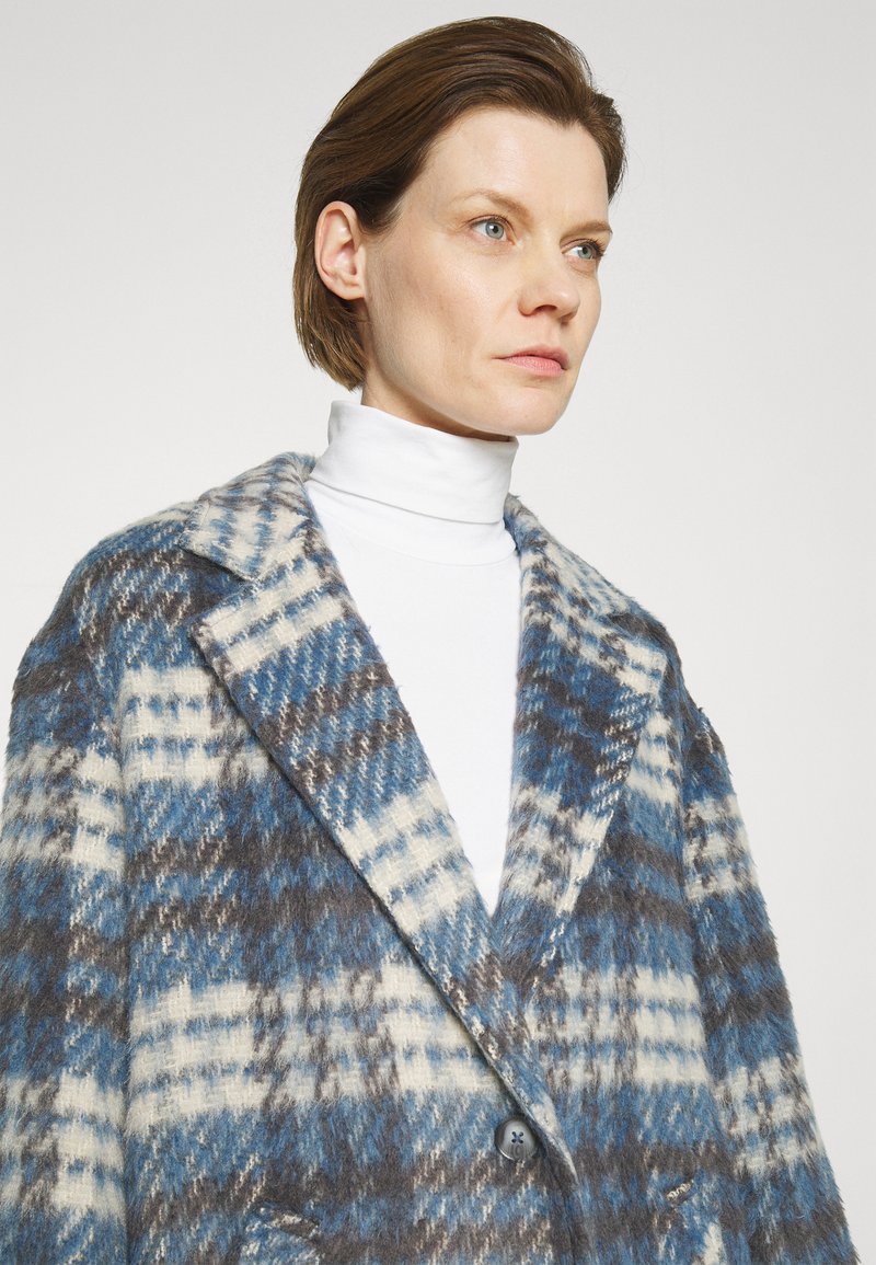 Abrigo oversize de mezcla de lana con un patrón de cuadros en azul, blanco y gris; con grandes solapas y cierre de un solo botón.