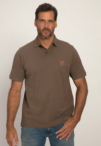 Ruskea polo-paita, jossa on kolmen napin kansi ja vasemmassa rinnassa pieni oranssi logo. Pehmeä puuvillainen materiaali, lyhyet hihat.