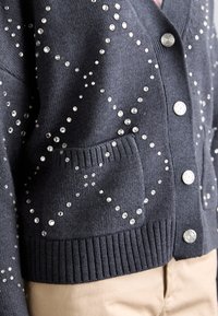 Tumehall cardigan tekstuuriga kudumist. Omab metallist nuppe ja jaotatud sädelevate kristallide kaunistusi kangal. Kaasa arvatud tasku.