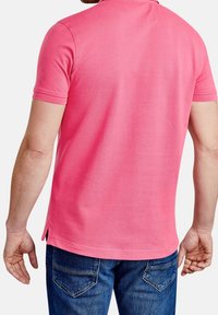 Różowa koszulka polo z krótkimi rękawami, z bocznymi rozporkami i klasycznym kołnierzykiem. Nosi ją z niebieskimi dżinsami. Gładka tekstura materiału.