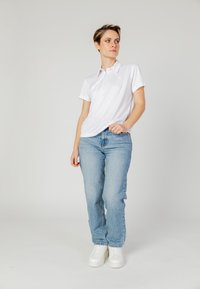 Polo bianco con un logo sottile, abbinato a jeans dritti blu chiaro e sneakers bianche. Tessuto morbido e vestibilità casual.