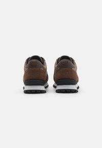 Braune Wildledersneaker mit einem strukturierten Obermaterial aus braunem Stoff, schwarzer Gummisohle und weißer Zwischensohle; Rückansicht, die die unterschiedlichen Materialien hervorhebt.