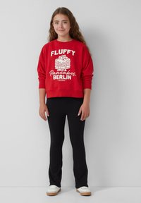 Rode sweatshirt met witte tekst en een pannenkoekafbeelding, gecombineerd met zwarte leggings en witte sneakers met een lichte zool.
