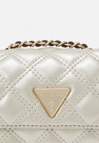 Pikowana srebrna torebka syntetyczna z trójkątnym złotym logo i paskiem na łańcuszku z czarnymi akcentami. Charakteryzuje się teksturowanym materiałem i kontrastującym przeszyciem.
