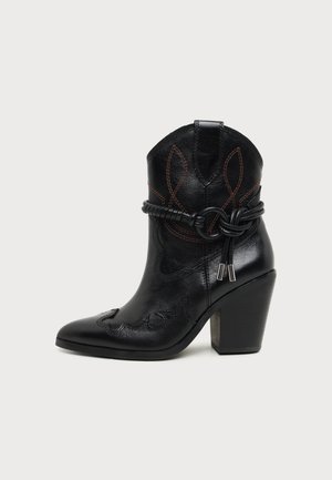 Black leather ankle cowboy boot with pointed toe, chunky heel, decorative stitching, and wrapped cord detail with metal tips.