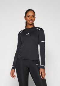 Langärmliges schwarzes Sportshirt mit reflektierenden Akzenten an Schultern und Ärmeln, das einen runden Halsausschnitt und ein schlankes, eng anliegendes Design aufweist.