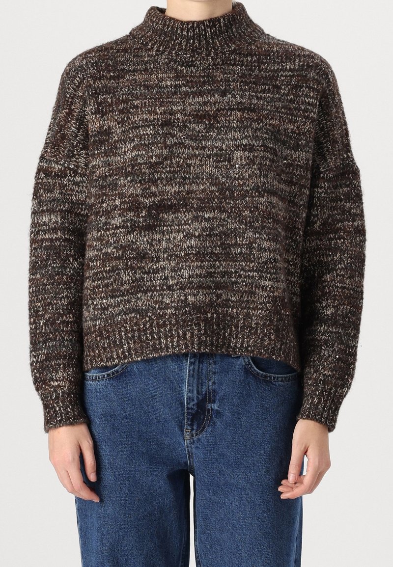 Brauner und grauer melierter Strickpullover mit hohem Kragen und lockerem Sitz, mit überschnittenen Schultern und gerippten Bündchen, kombiniert mit blauen Jeans.