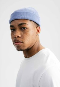 Lichtblauwe gebreide beanie met een geribbeld patroon en een opgerolde boord, gedragen door een persoon in een wit T-shirt met ronde hals, tegen een effen achtergrond.