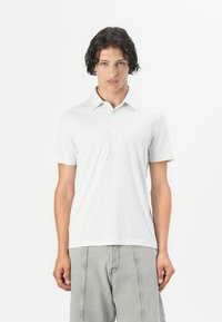 Polo de manga corta en gris claro con un patrón geométrico, fabricado en una tela suave. Presenta un collar y una tapeta de botones.