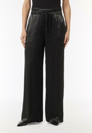 Wide-leg black leather pants with a high elastic waist and drawstring, worn with black pointed shoes and a black top.