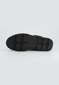Semelle de chaussure en caoutchouc noir avec des motifs de texture pour une meilleure adhérence et un logo en relief. Elle pr ésente un design large et plat pour une stabilité et une traction optimales.