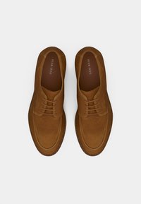 Καφέ σουέντ παπούτσια με λεία επιφάνεια, διαθέτουν στρογγυλερή μύτη, δέσιμο με κορδόνια και μίνιμαλ λεπτομέρειες. Το λογότυπο της μάρκας είναι ορατό στο εσωτερικό.