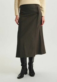 Jupe midi rayée brune en tissu texturé, avec une fermeture à boutons sur le côté et une taille haute. Portée avec des bottes noires jusqu'aux genoux.