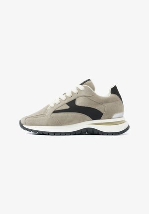 Suede sneakers in light beige with a black mesh side panel. Features white laces and a cushioned white and black sole. Classic athletic design.