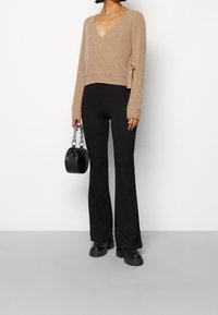 Beige omslagströja med V-hals, långa ärmar, kombinerad med svarta utsvängda byxor och kraftiga svarta skor. Liten svart handväska med metalliska detaljer.