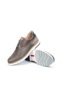 Chaussures en cuir brun clair avec une surface perforée, accents de talon noir, lacets gris et semelle en caoutchouc blanc avec un motif de semelle.