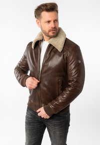 Giubbotto di pelle marrone con colletto in shearling, polsini e orlo a costine. Presenta una chiusura frontale con zip e tasche laterali. Design vintage e testurizzato.